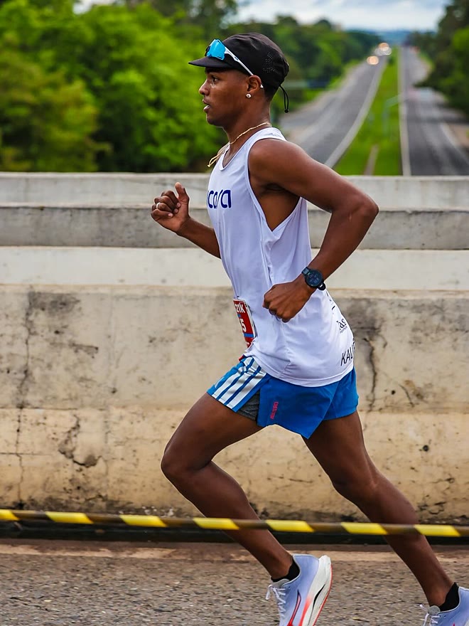 Kauê de Souza de perfil, em passada aberta sobre a ponte da rodovia, na Meia Maratona de Americana