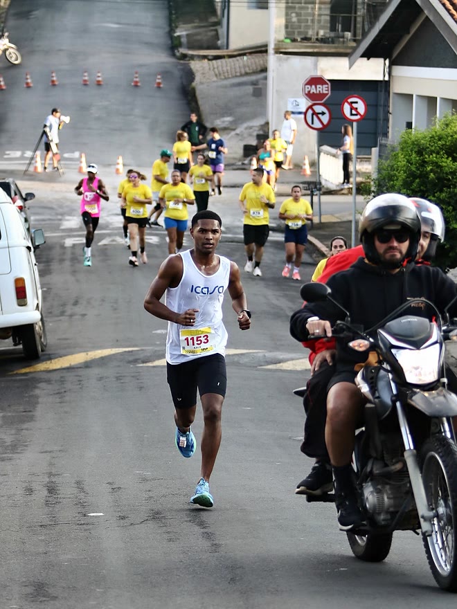 Kauê de Souza na frente da prova, com a moto de apoio ao lado e o pelotão ao fundo, na 2ª Corrida do Café