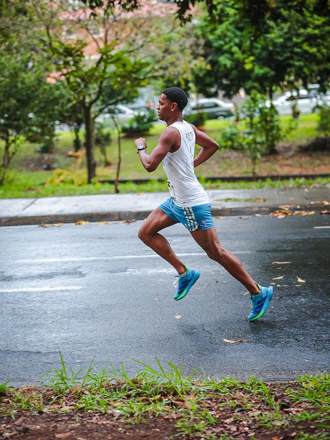 Kauê de Souza de perfil, em passada aérea sobre o asfalto molhado, na 5ª Corrida Sônia Esportes