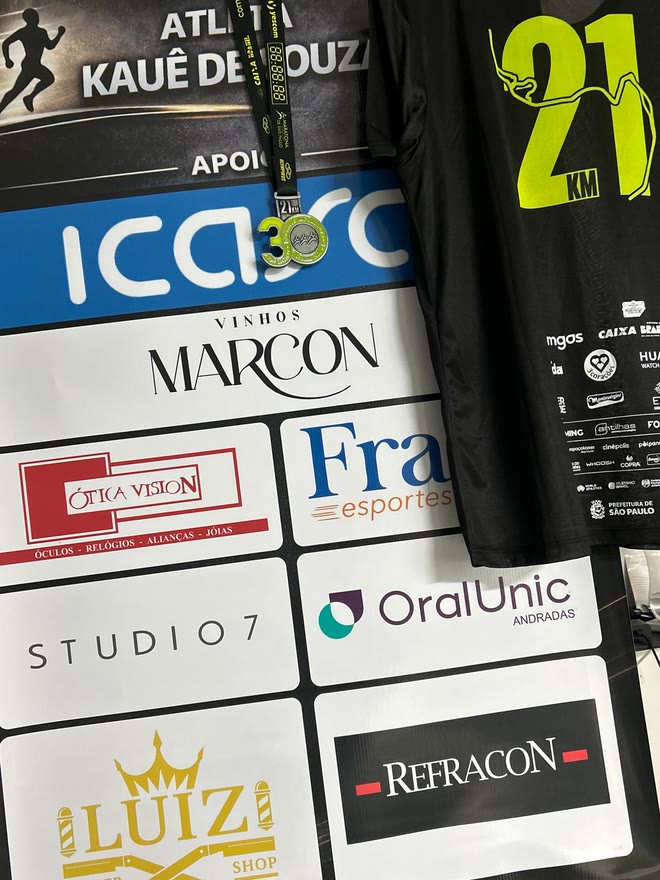 Medalha dos 21 km da Maratona Internacional de São Paulo sobre o banner de patrocinadores do atleta, ao lado da camiseta oficial da prova
